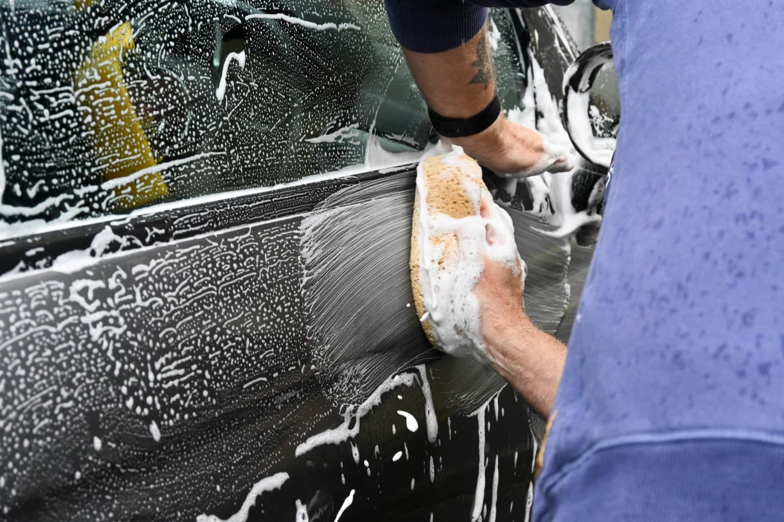 Hand washing a soapy car door with a sponge